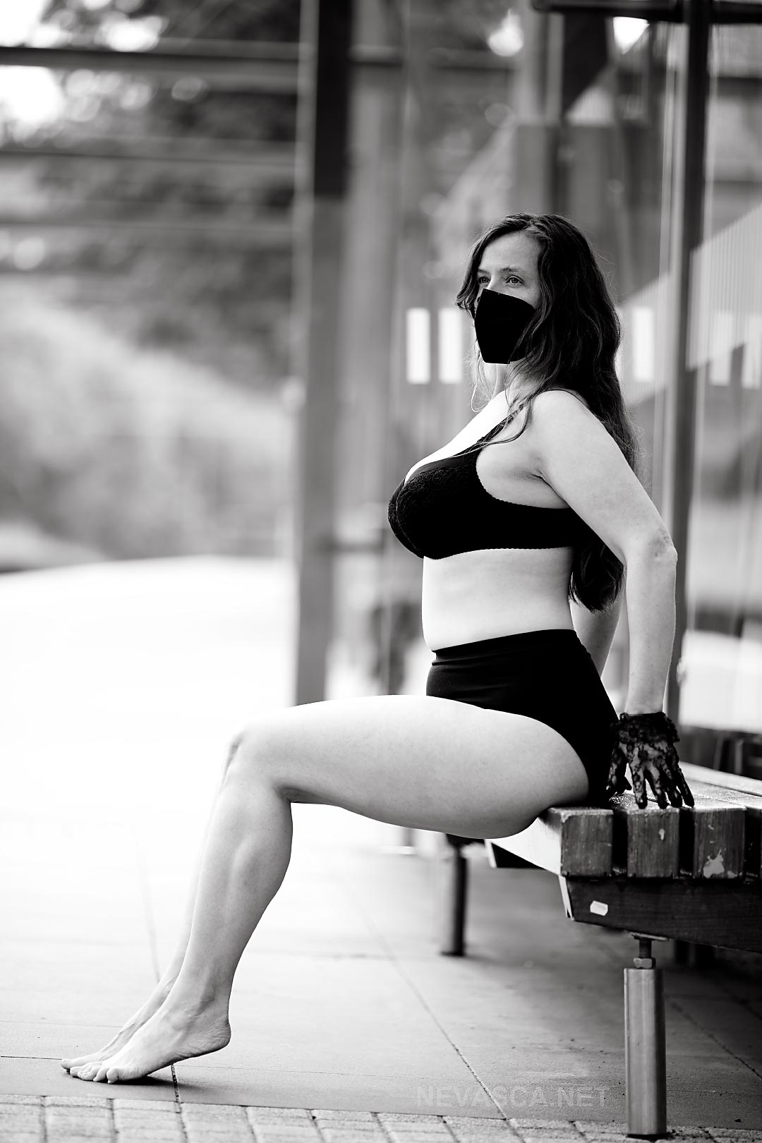 Eine Frau mit Maske sitzt auf einer Bank in einer Haltestelle.