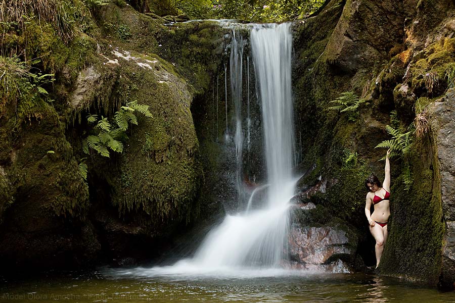 A woman wearing swimwear is standing beside a waterfall.