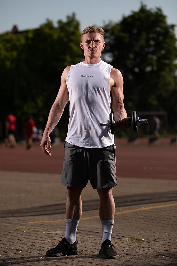 A man standing in a park is holding a dumbbell.