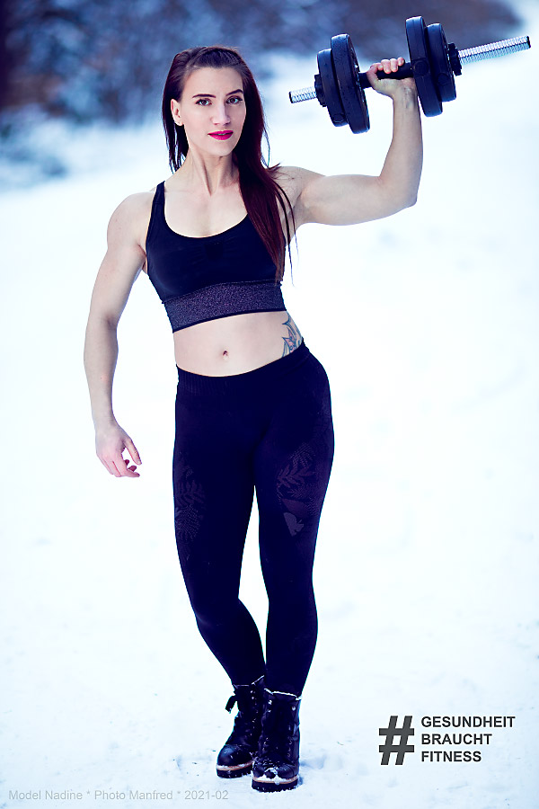 A young woman standing outside in a snowy landscape is holding a dumbbell.