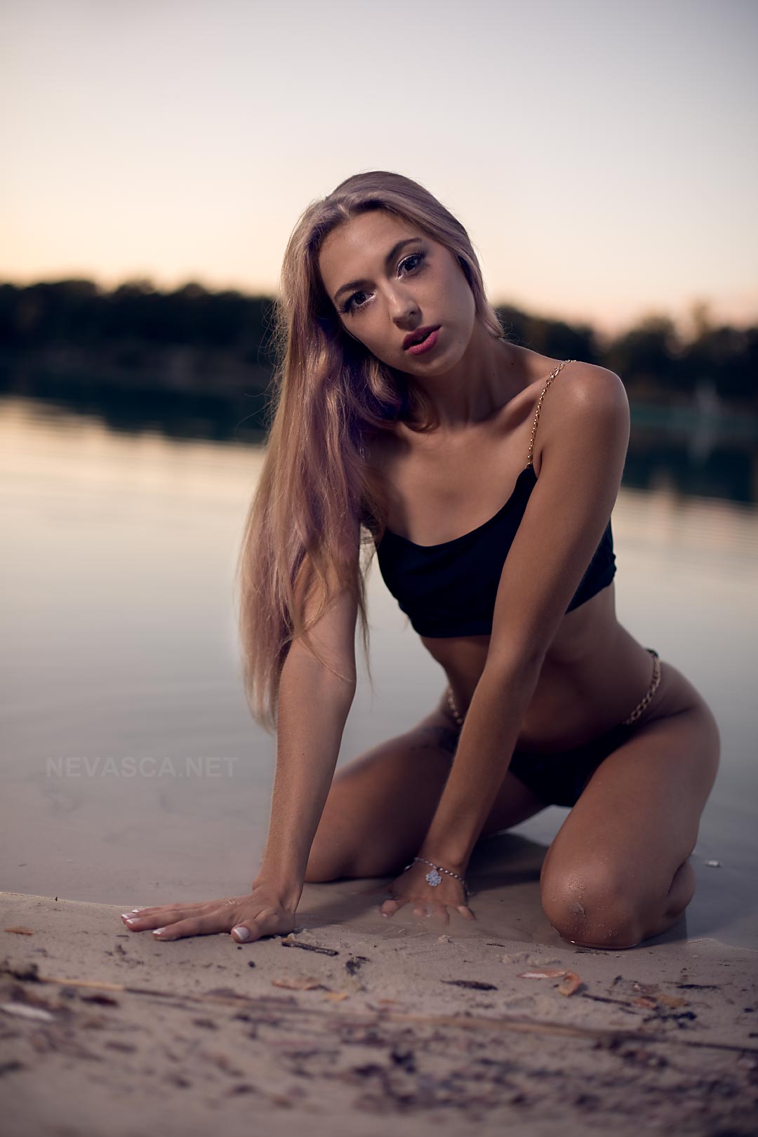 A young woman wearing black swimwear is sitting in front of a lake.