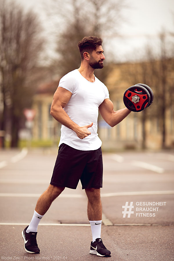 A young man standing in a parking space is holding a dumbbell.